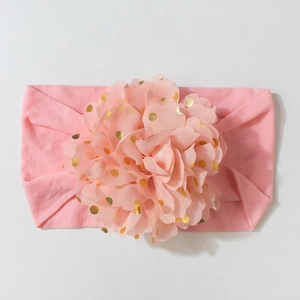 Gros plan d'un bandeau rose pour bébé avec grande fleur en tulle et pois dorés