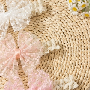 Detailed view of delicate lace bow headbands for babies with floral embroidery on woven mat