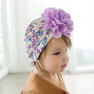 Détail d'un bonnet floral pour bébé avec grande fleur en mousseline mauve et pois dorés