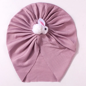 Détail d'un bonnet côtelé pour bébé avec un lapin en peluche blanc sur un fond de tissu rose