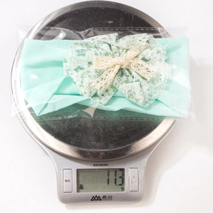 Detail showing mint green nylon baby headband with lace bow weighing 11.3g on a scale