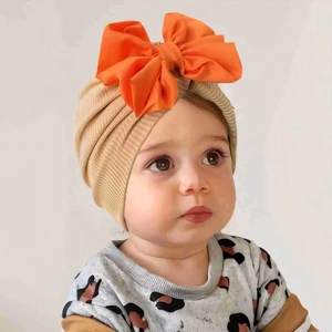 Close-up of soft ribbed baby turban headband featuring a large bright orange bow detail