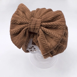 Detail of baby knit hat featuring a large bow and vintage cable knit texture in brown