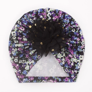 Détail du bonnet floral pour bébé avec une grande fleur noire 3D et des pois dorés