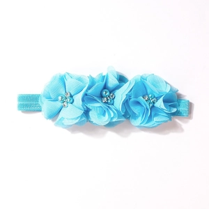Dettaglio di fascia per neonati celeste con fiori in chiffon, perle e strass scintillanti
