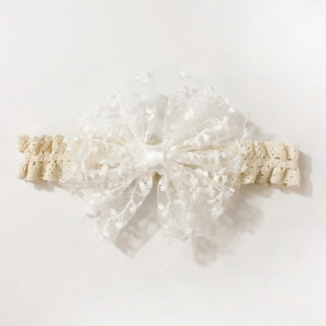 Close-up of white lace bow headband for babies with floral embroidery and mesh detail
