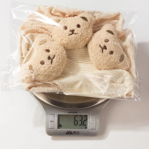 Baby cream socks set with plush bear decor on digital scale showing total weight of 63.2g