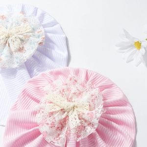 Détail de bonnets bébé avec grandes fleurs en dentelle et nœuds sur tissu côtelé