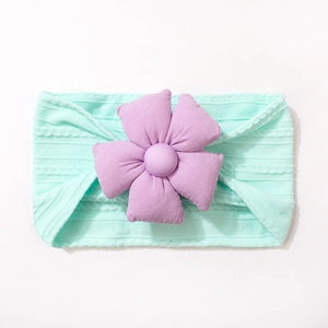 Détail d'un bandeau bébé en tricot vert menthe avec une grande fleur en tissu mauve