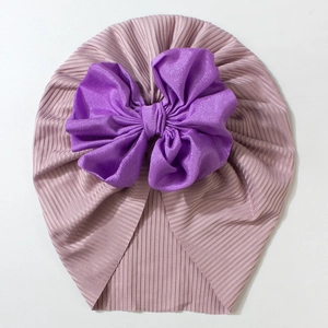 Detailed close-up of pink ribbed baby beanie featuring a large purple bow decoration