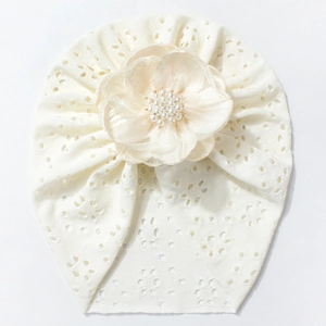 Detail einer Baby-Turban-Mütze aus Eyelet-Stoff mit großer Perlenblume in Cremeweiß