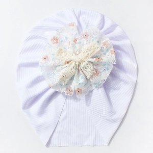 Détail d'un bonnet bébé côtelé blanc avec fleur en dentelle florale et nœud tissé