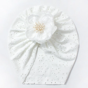 Detail eines weißen Baby-Turbans mit hohler Spitze, großer Netzblume und Perlenverzierung