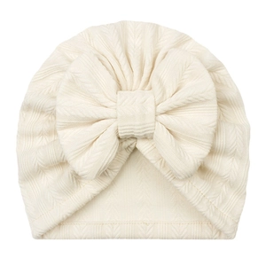 Detail of baby beanie featuring wheat ear knit texture and a large cream-white bow