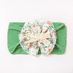 Detail of baby nylon headband with floral lace and beige crochet bow on green fabric
