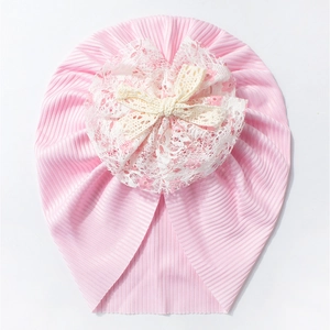 Détail d'un bonnet bébé côtelé rose avec fleur en dentelle blanche et nœud au crochet