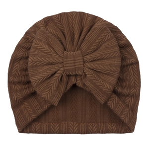 Detailed view of the thick cable knit texture and large bow on this brown baby turban hat