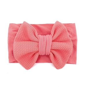 Close-up of coral pink infant headband with a textured large bow on a soft elastic band