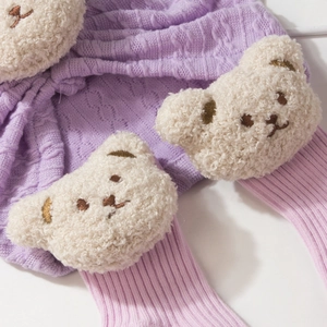 Detail view of purple knit baby leggings featuring a plush 3D fleece bear patch