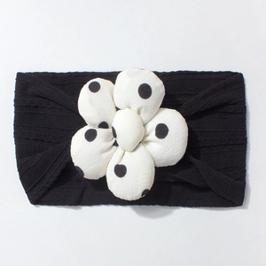 Detail of baby headband featuring black ribbed knit fabric and large white polka dot flower
