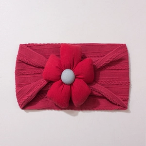 Détail d'un bandeau pour bébé en tricot rouge foncé avec une grande fleur en tissu doux
