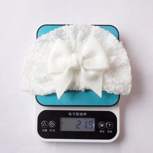 Lightweight white waffle knit baby hat with bow weighing only 21.9g on a digital scale