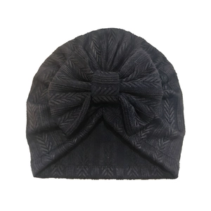 Detailed view of black knitted baby turban hat with soft herringbone pattern and large bow