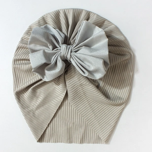 Detail of baby ribbed knit turban featuring a large soft grey satin bow on beige fabric