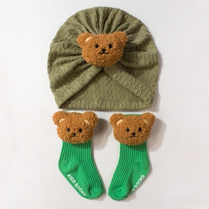 Close-up of olive green knitted baby hat with plush bear and ribbed matching socks