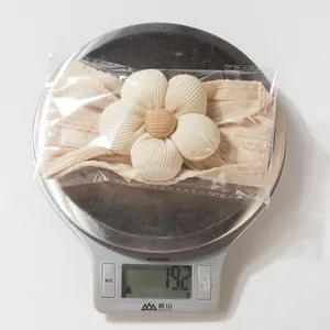 Close-up of baby beige knit flower headband in packaging on a scale weighing 19.2g