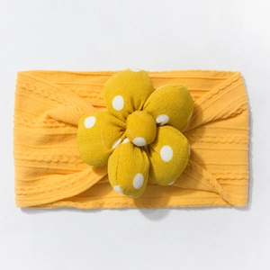 Detail of yellow knitted baby headband featuring a large polka dot 3D flower decoration