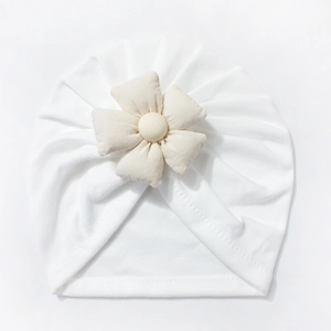 Detail of soft white knit baby hat with a decorative cream fabric flower on white background