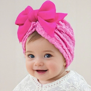 Detailed view of pink breathable infant turban hat with a large satin bow on a smiling toddler