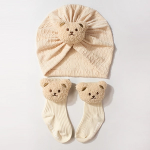 Close-up of beige baby hat and socks set featuring 3D plush bear ears on soft knit fabric