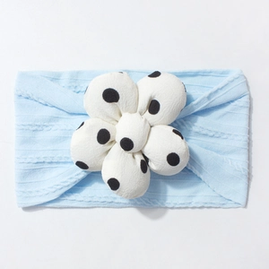 Detail of light blue ribbed knit baby headband featuring a plush white polka dot flower