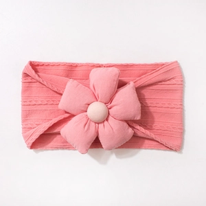 Détail d'un bandeau en tricot rose pour bébé avec une grande fleur décorative en tissu