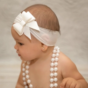 Detail of soft white nylon baby headband featuring a large textured bow and elastic band