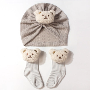 Detailed view of grey knitted baby hat and socks set featuring cute plush bear accents