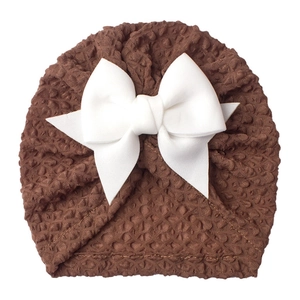 Detail of soft brown waffle knit baby hat featuring a large white decorative satin bow