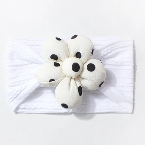 Detail of soft white baby headband featuring a 3D floral accent with black polka dots
