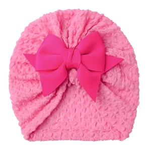Pink waffle knit baby turban hat featuring a large decorative satin bow on a white background