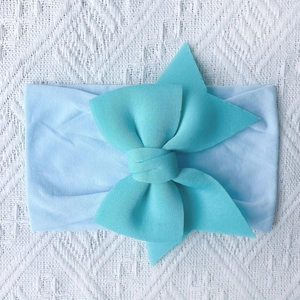Close-up of tiffany blue infant headwrap with a large decorative bow on white lace cloth