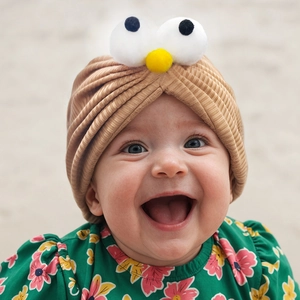 Gros plan du bonnet turban bébé avec de grands yeux de dessin animé et pompons jaunes