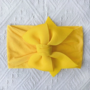 Detail of soft yellow nylon baby headband with large double-layered bow on white knit