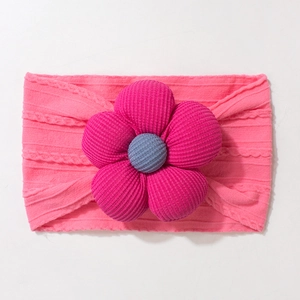 Detailed close-up of pink knitted baby headband with a large 3D fabric flower and ribbed texture