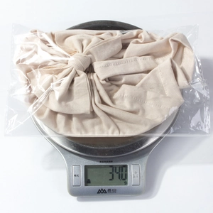 Beige ribbed bow baby hat packaged for quality check weighing 34g on a scale