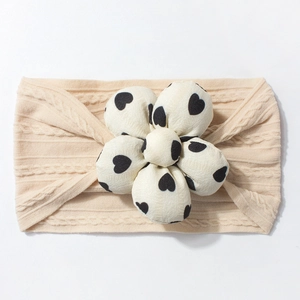 Detail view of beige knitted baby headband with a large black heart pattern floral accent