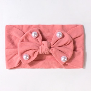 Dettaglio della fascia rosa per neonati con fiocco grande e perle bianche su tessuto