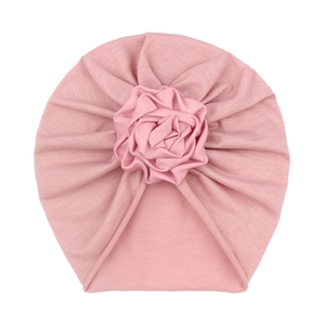 Detail of baby turban hat featuring a handcrafted soft pink rose and knitted fabric texture