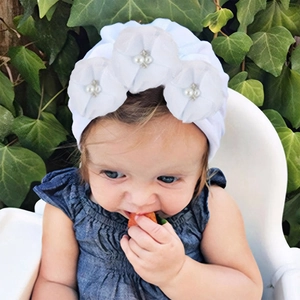 Détail d'un bonnet turban blanc pour bébé avec fleurs, perles et strass brillants